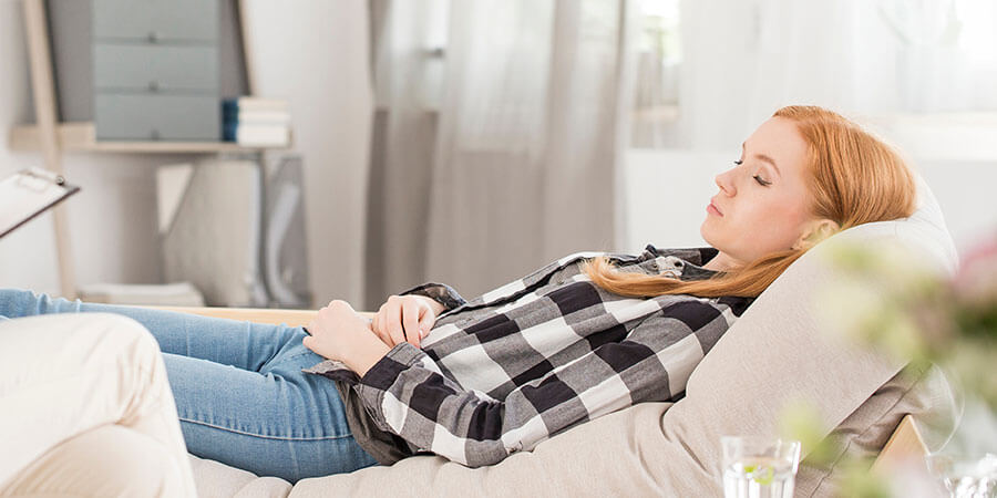 Hypnose Reinach | Frau liegt auf Couch mit geschlossenen Augen. Links macht sich Therapeut Notizen