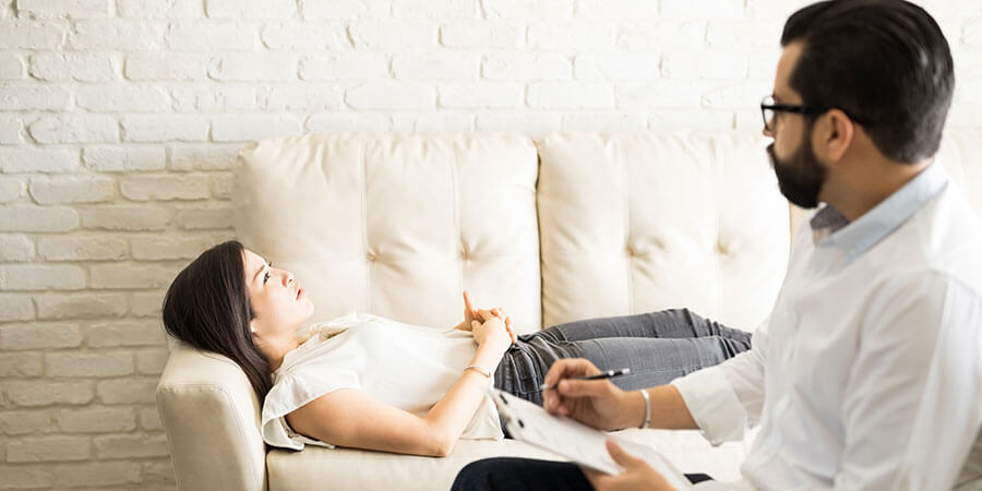 Hypnose Limmattal | Frau liegt auf Couch mit offenen Augen. Rechts im Vordergrund der Therapeut