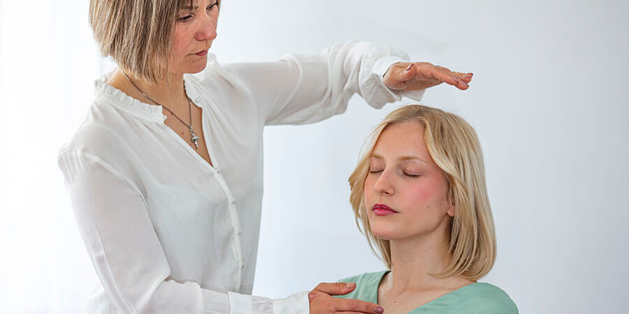 Hypnose Cham | sitzende Frau, Die Therapeutin hält eine Hand über sie und berührt mit der anderen die Schulter