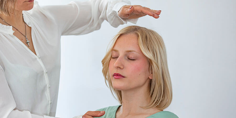 Hypnose Limmattal | sitzende Frau, Die Therapeutin hält eine Hand über sie und berührt mit der anderen die Schulter