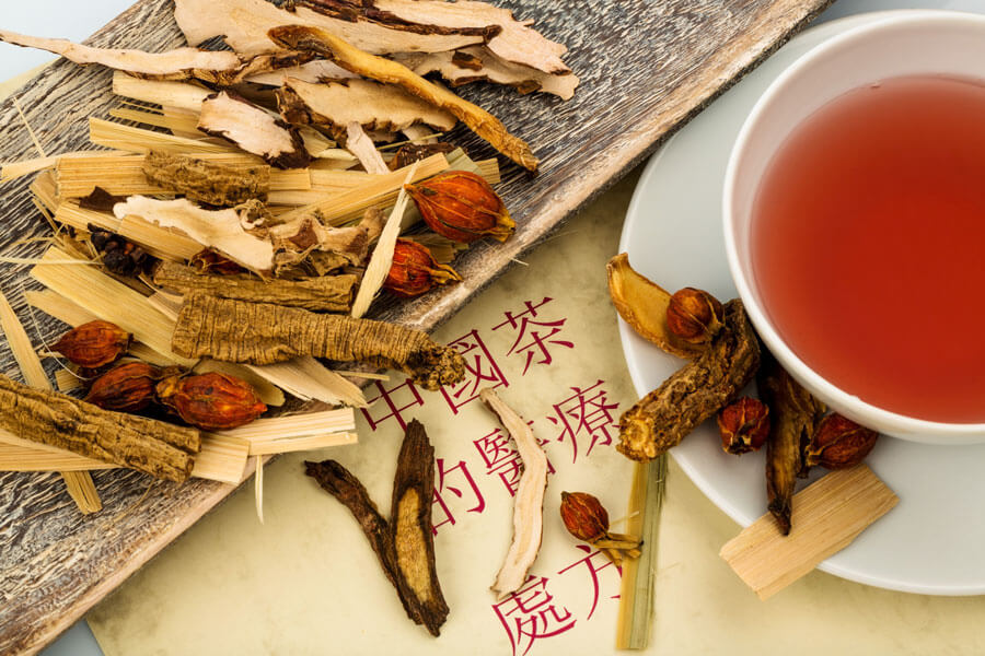 Traditionelle Chinesische Medizin in Luzern | Kräuter auf Holzbrett neben rotem Tee