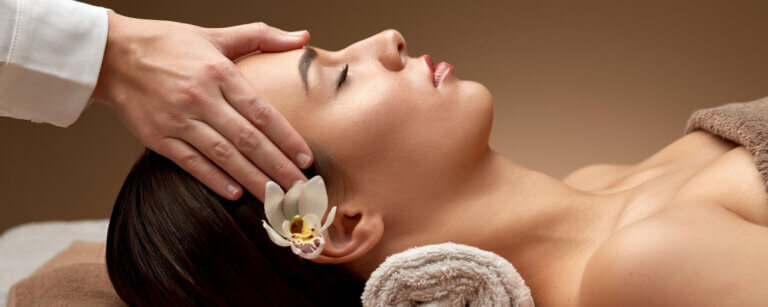 Shiatsu in Baden | Frau mit Blume im Haar liegt auf Massageliege und wird manuell am Kopf behandelt